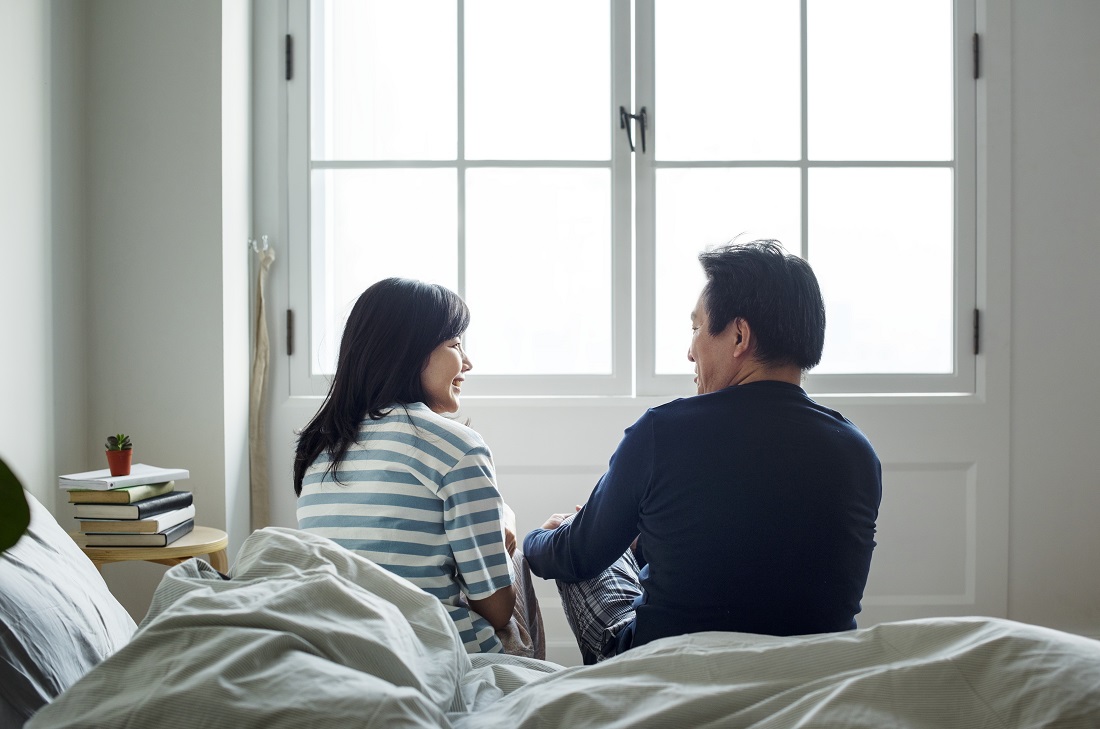 Couple sitting on the edge of the bed looking at each other.